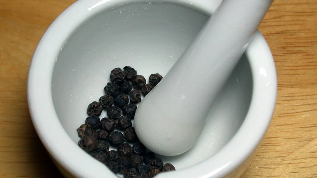 Whole black peppercorns (Piper nigrum) in a mortar with pestle